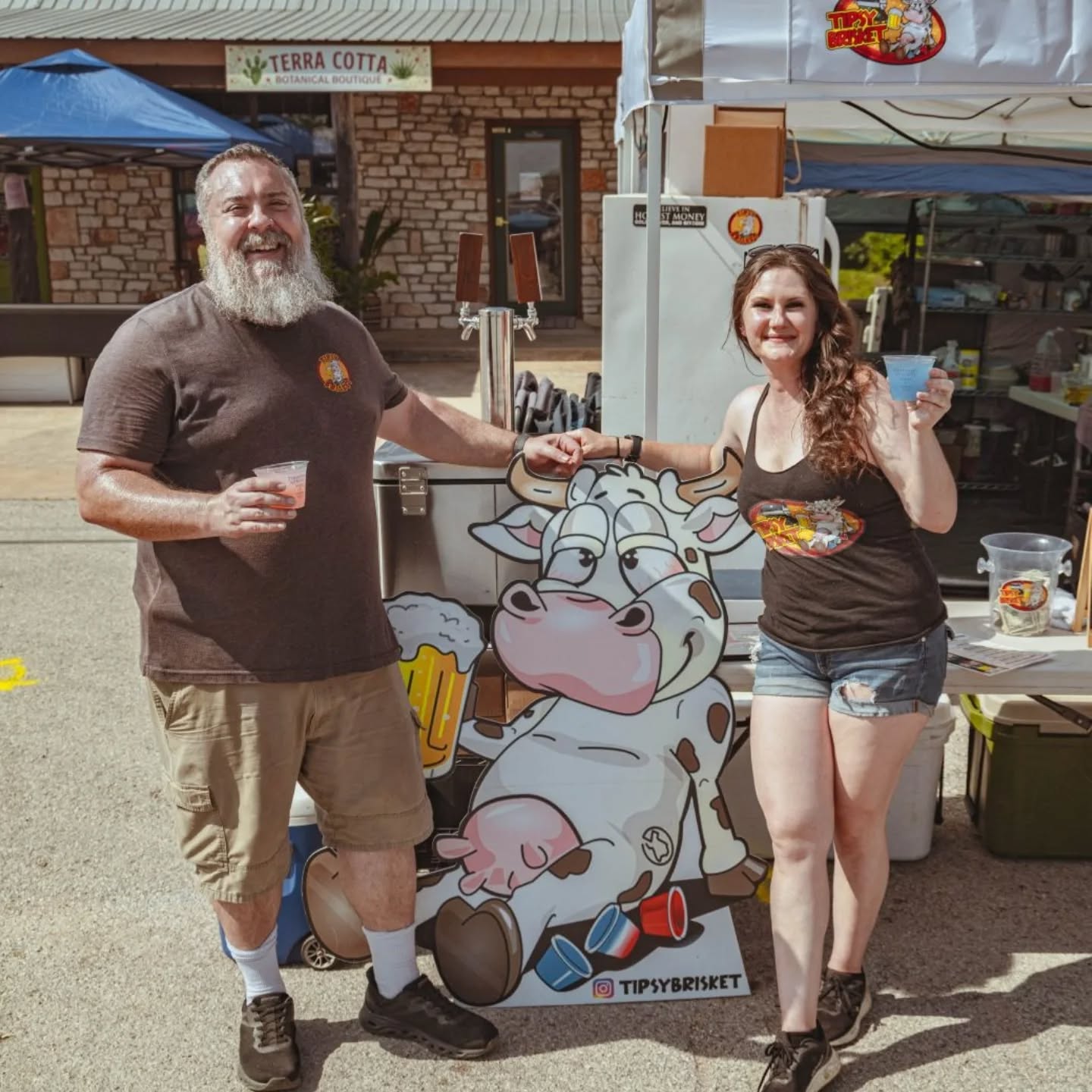 Chris and Noella Olds at the Tipsy Brisket tent with the cow cutout between them